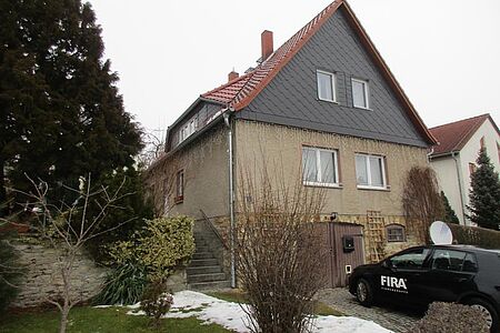Wohnhaus mit dunkelgrau vertäfeltem ersten Stock, verschmutzter Fassade im Erdgeschoss und Klinkern im Untergeschoss