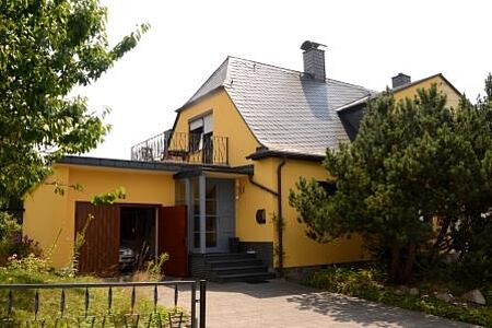 Haus mit kräftig gelber Fassade und kleinem Balkon auf dem Anbau