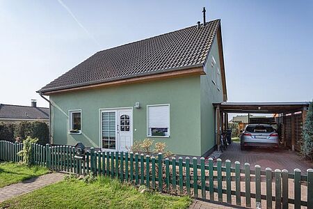Grünes Wohnhaus mit angebautem Holzcarport