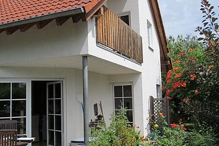 Wohnhaus mit weißer Fassade und Balkon mit Holzgeländer