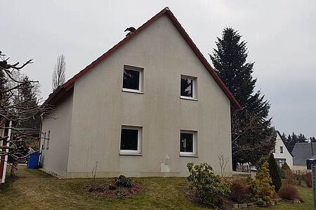 Weißes Einfamilienhaus mit starken Witterungsspuren an der Fassade