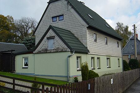 Haus mit grünem Putz und Vertäfelung in den oberen Stockwerken