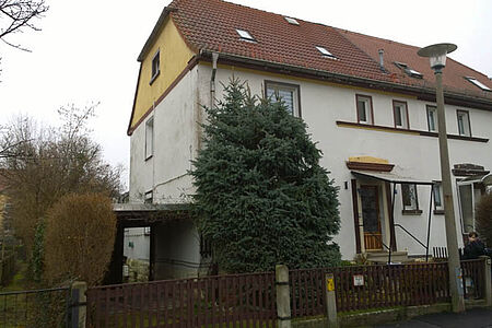 Mehrstöckiges Wohnhaus mit verwitterter, weißer Fassade vor der Sanierung