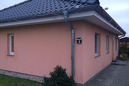 Bungalow mit schwarzem Walmdach und Feuchtigkeitsflecken auf der korallefarbenen Fassade