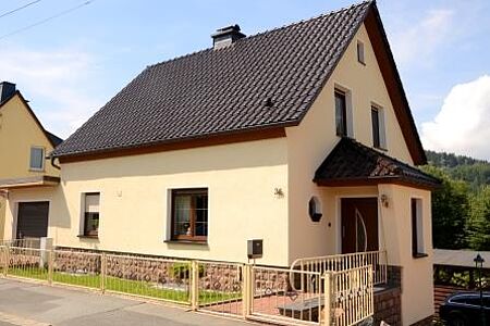 Kleines Einfamilienhaus mit sandgelber Fassade und kleinem Vorgarten