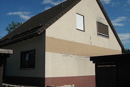 Einfamilienhaus mit Satteldach und verschmutzter Fassade in verschiedenen Brauntönen