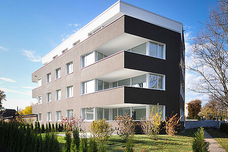 Graues Mehrfamilienhaus in einer Grünanlage