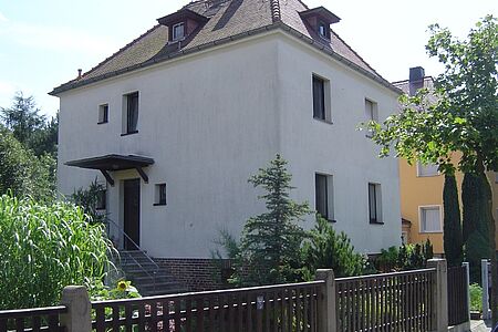 Ehemals weißes, mehrstöckiges Wohnhaus mit leicht ergrauter Fassade vor der Sanierung