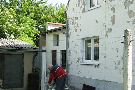 Älterer Herr vor einer beschädigten weißen Fassade.