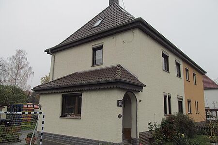 Weiße Doppelhaushälfte mit Witterungsspuren und Walmdach