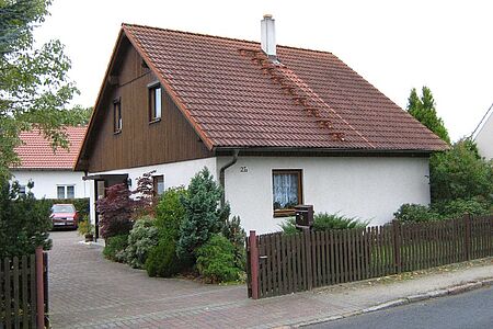 Einfamilienhaus mit weißer Fassade im Erdgeschoss und dunkelbrauner Holzvertäfelung im Obergeschoss